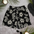 Black athletic shorts with cream floral and paisley print, displayed with palm leaves and sunglasses.