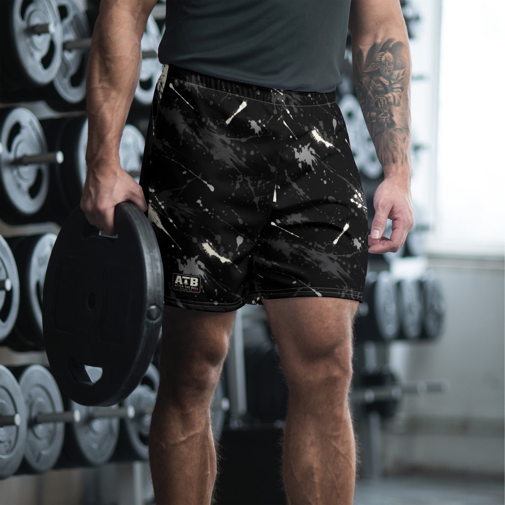 Man wearing black athletic shorts with white and gray paint splatter and a dark workout shirt in a gym.