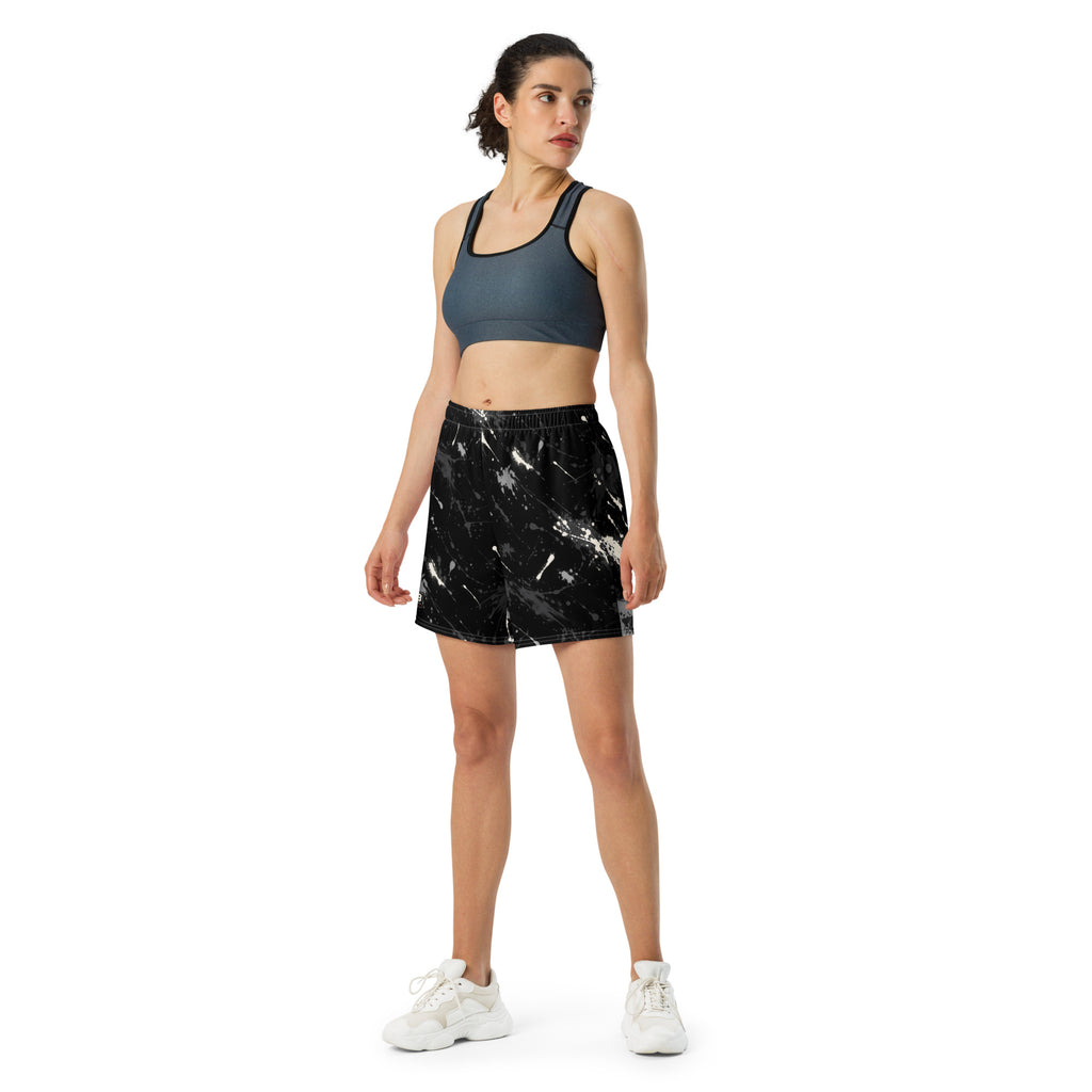 Woman wearing black splatter-print athletic shorts with a dark sports bra and white sneakers.