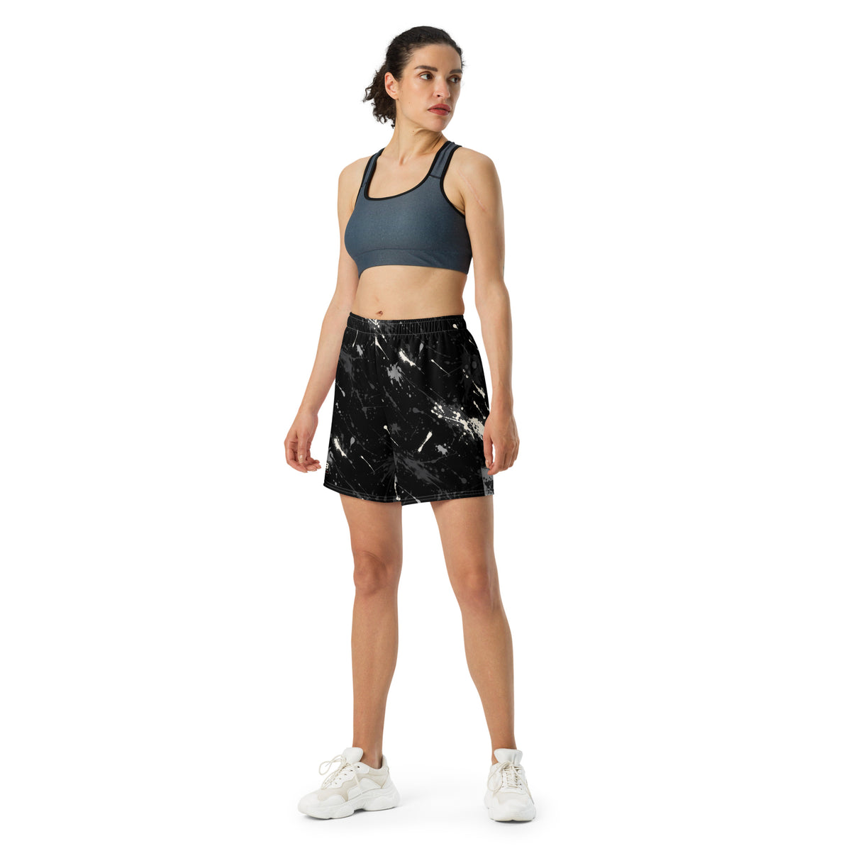 Woman wearing black splatter-print athletic shorts with a dark sports bra and white sneakers.