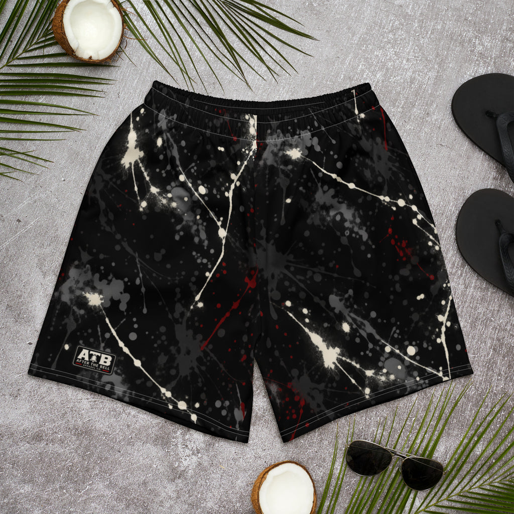 Front view of black athletic shorts with white and red paint splatter and a small ATB logo, laid flat on a gray surface.
