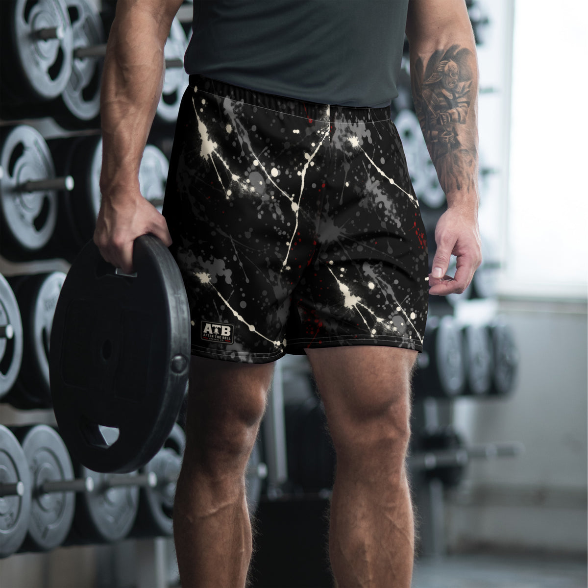 Man wearing black athletic shorts with white and red paint splatter and a dark workout shirt in a gym.