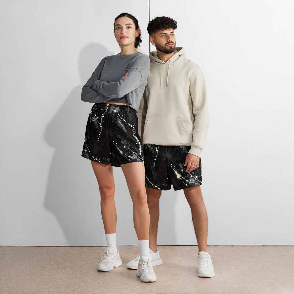 Two models wearing black splatter-print athletic shorts with casual tops and white sneakers.