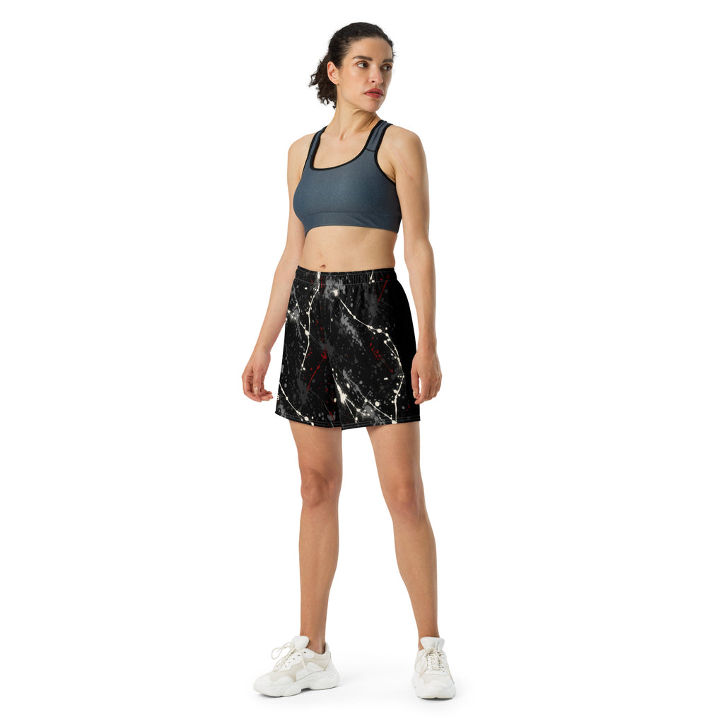 Woman wearing black splatter-print athletic shorts with a dark sports bra and white sneakers.