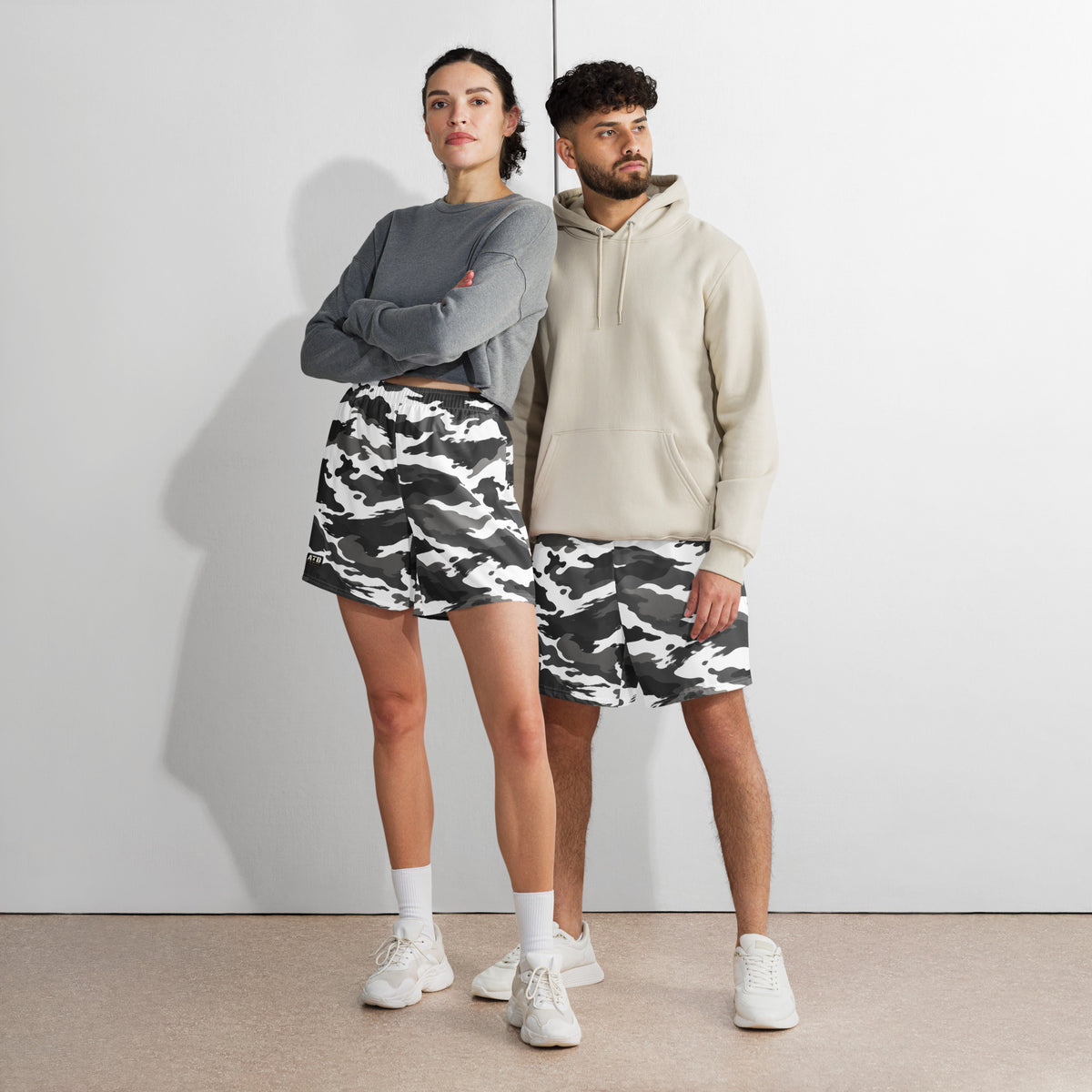 Two models wearing white camouflage athletic shorts with casual tops and white sneakers.