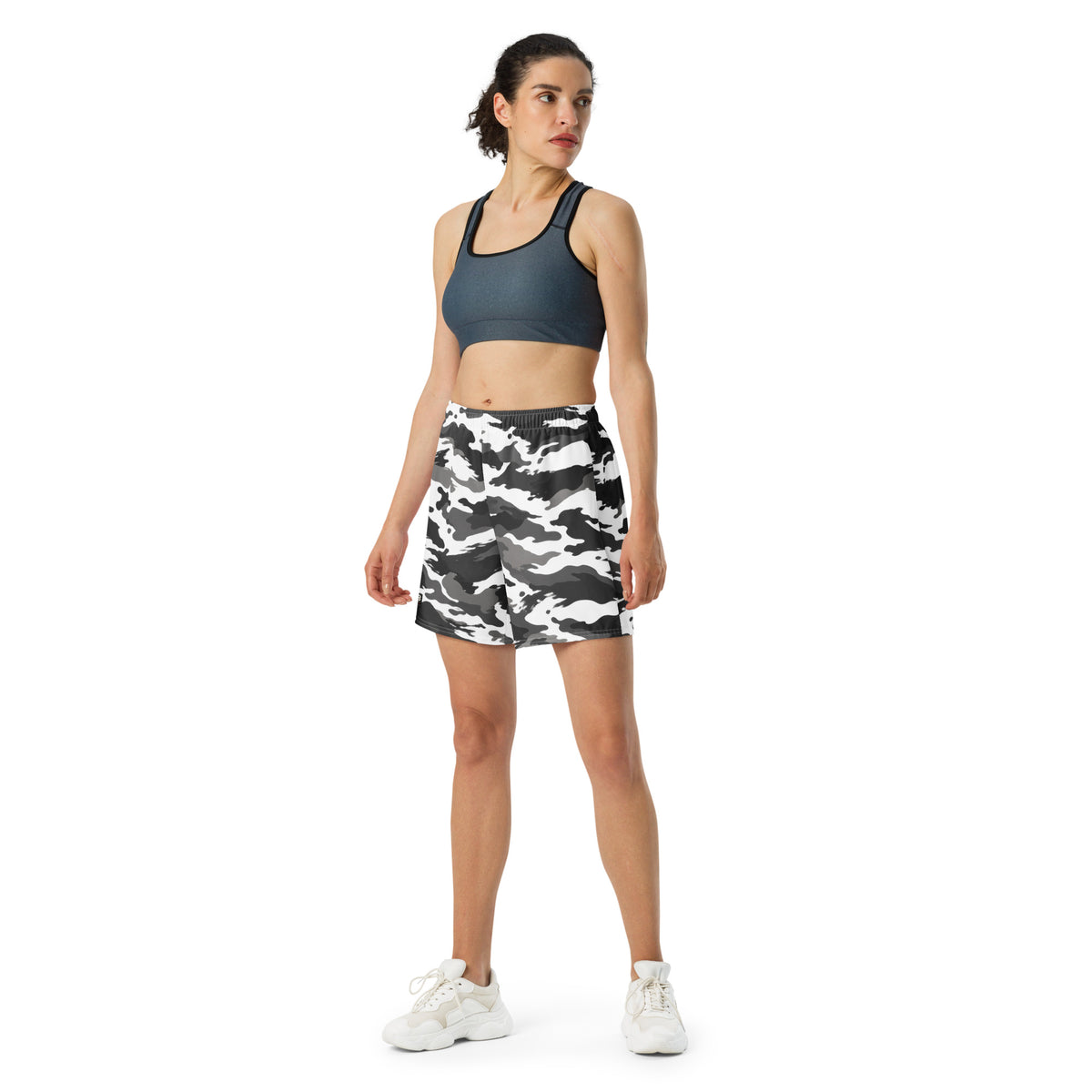 Woman wearing white camouflage athletic shorts with a dark sports bra and white sneakers.