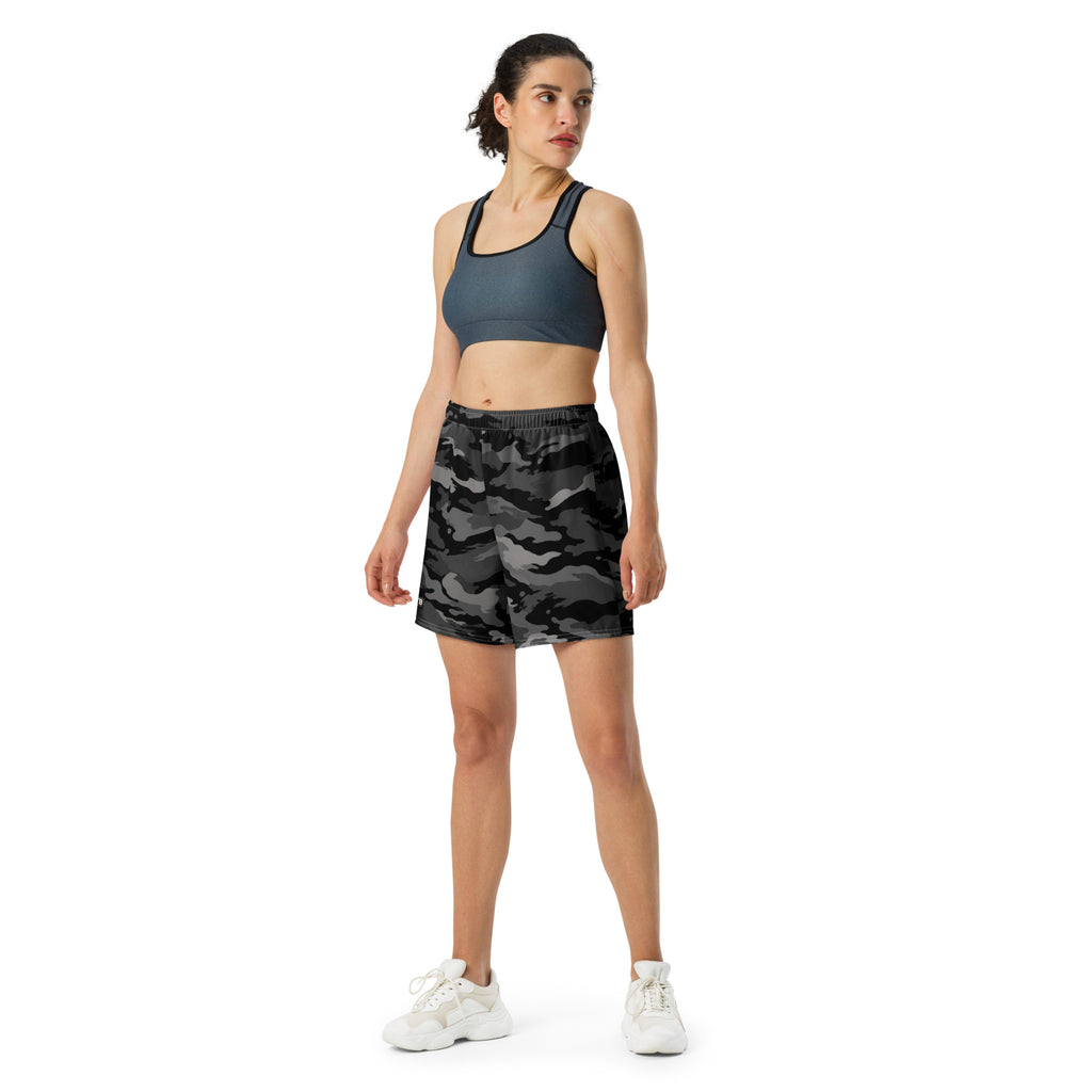 Woman wearing black camouflage athletic shorts with a dark sports bra and white sneakers.