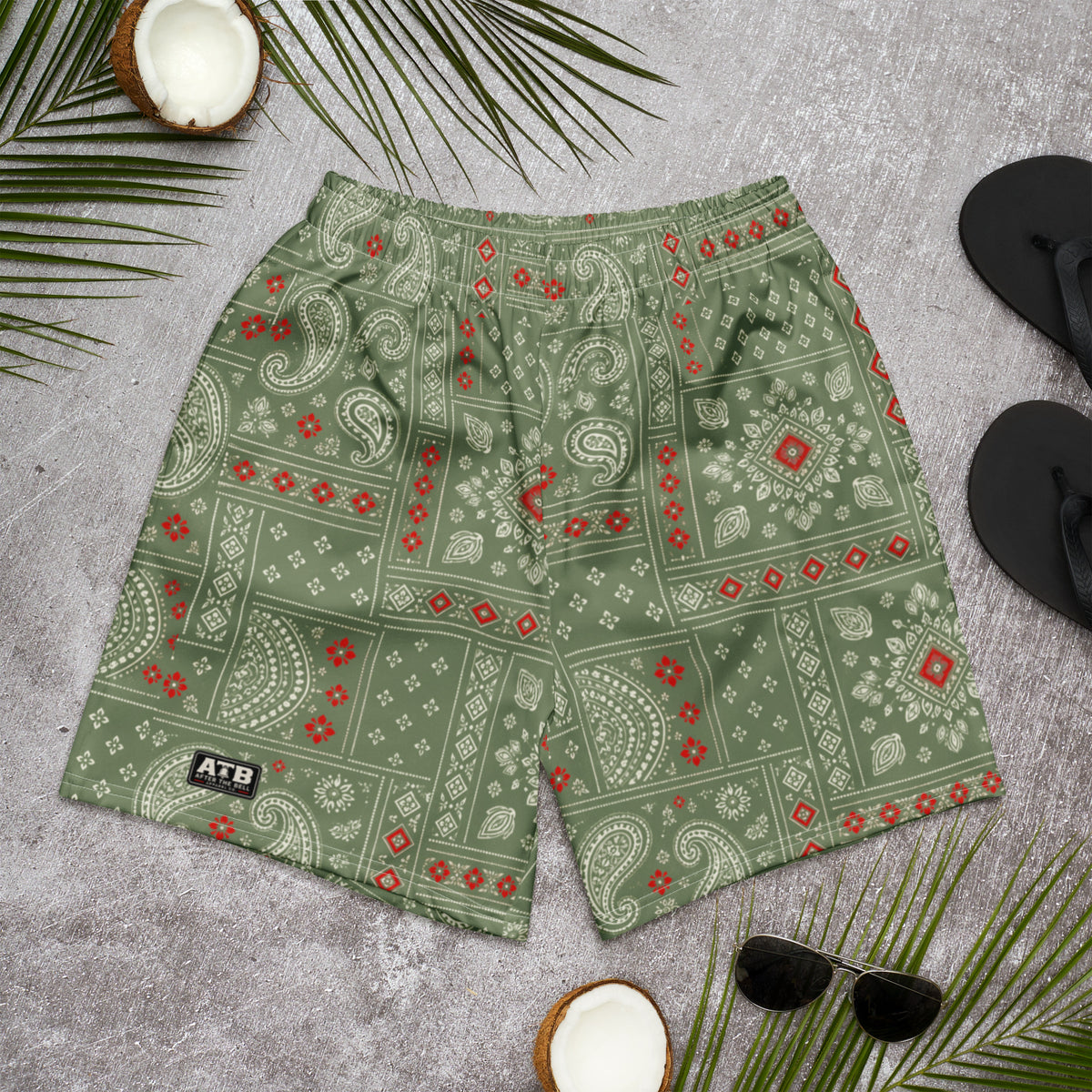 Camo green athletic shorts with cream paisley and red bandana accents, laid flat on a gray surface.