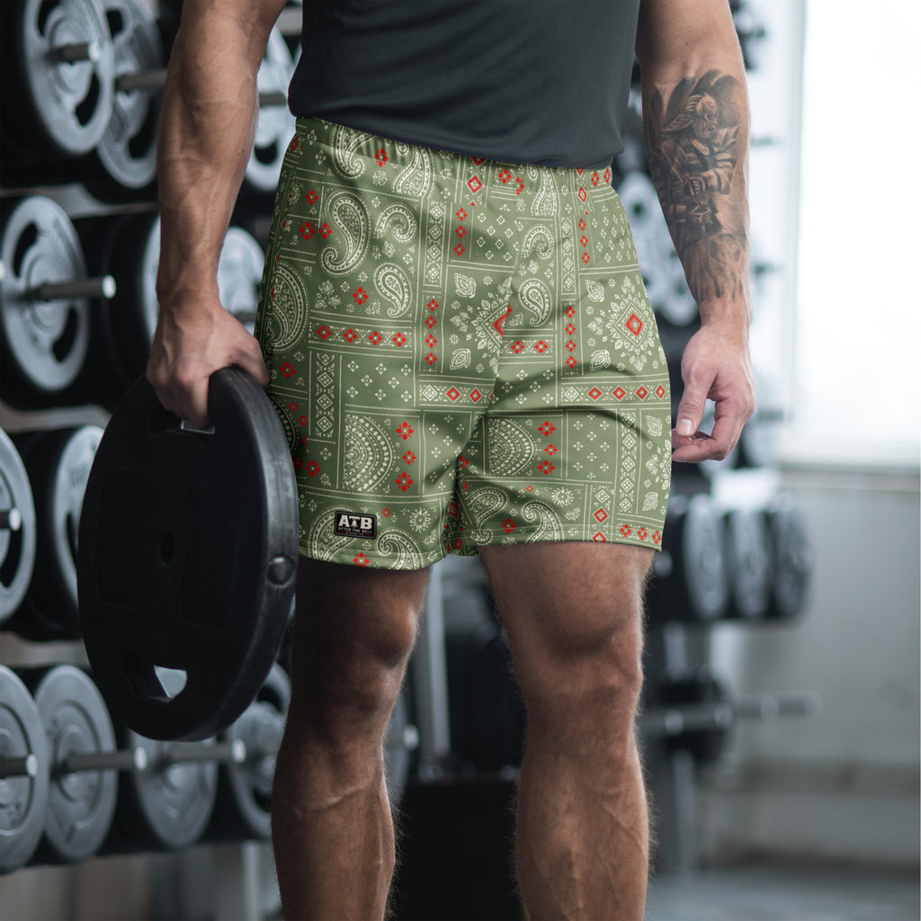 Man wearing camo green bandana-print athletic shorts and a dark workout shirt in a gym.