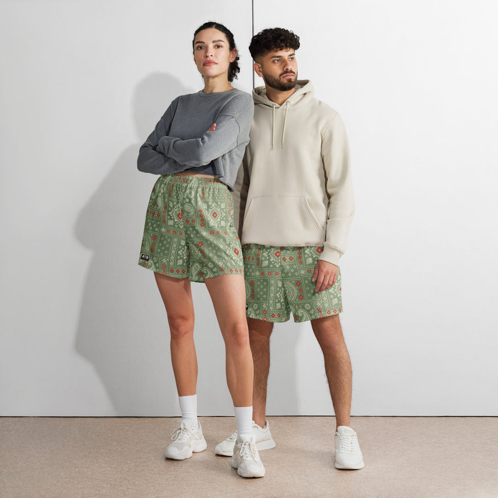 Two models wearing camo green bandana-print athletic shorts with casual tops and white sneakers.