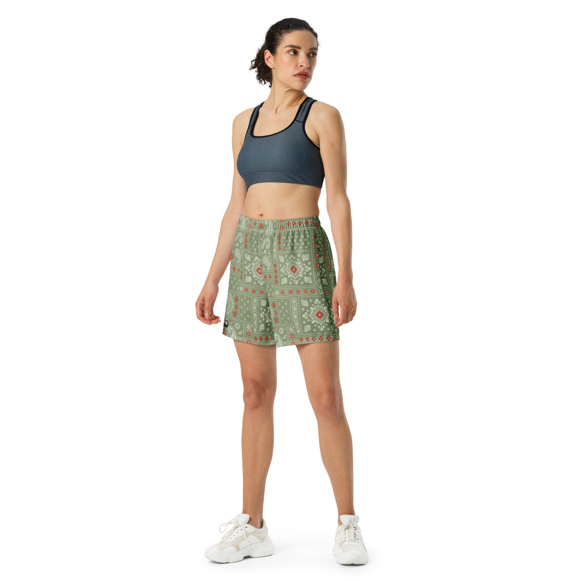 Woman wearing camo green bandana-print athletic shorts with a dark sports bra and white sneakers.