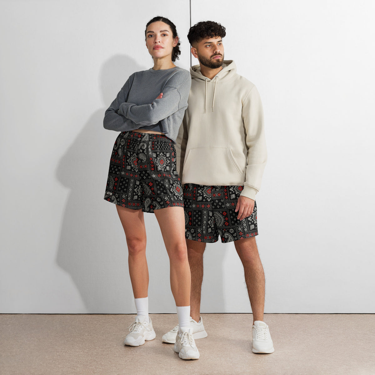 Two models wearing black bandana-print athletic shorts with casual tops and white sneakers.