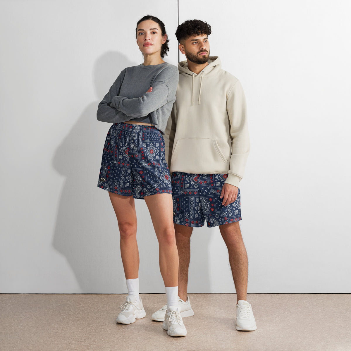 Two models wearing navy bandana-print athletic shorts with casual tops and white sneakers.