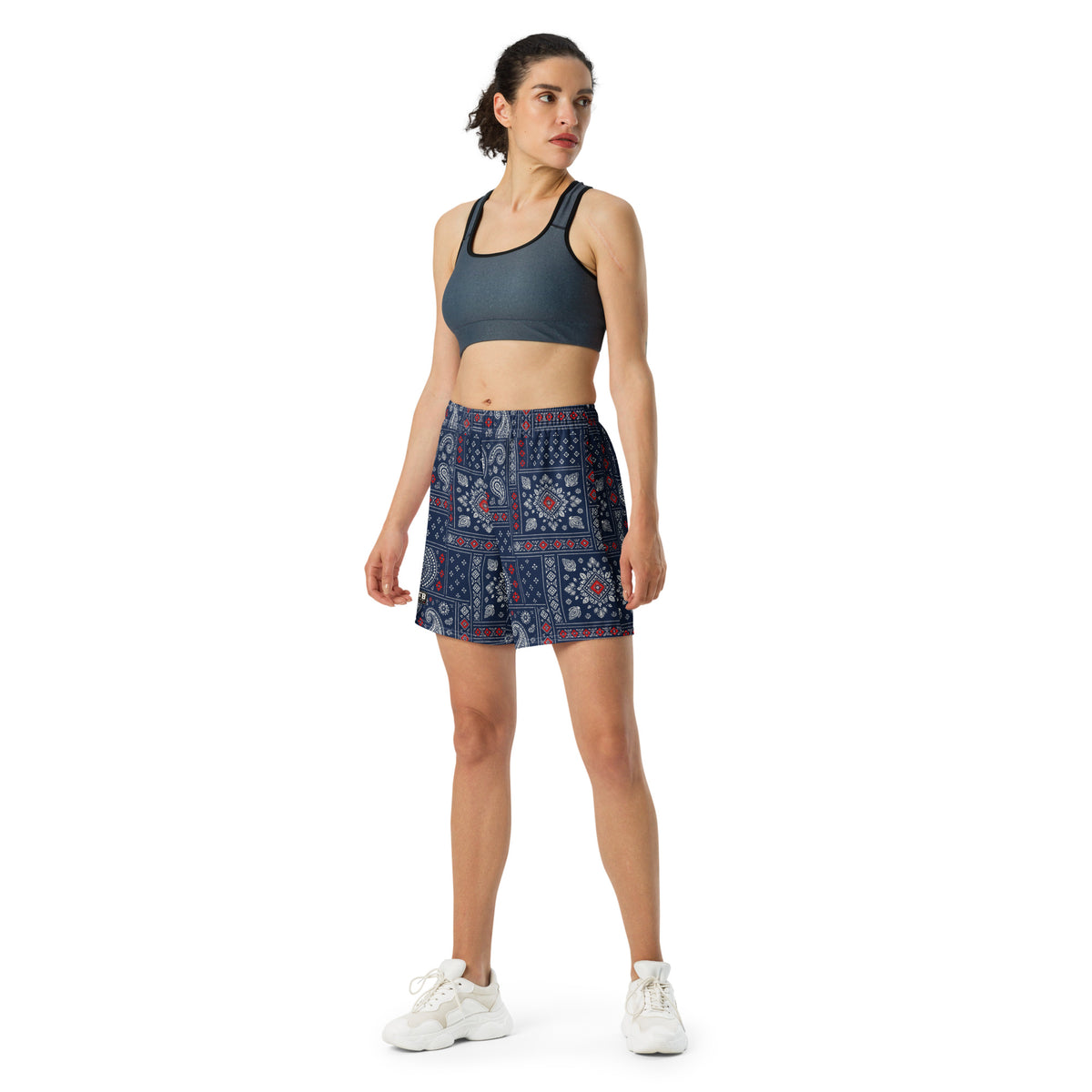 Woman wearing navy bandana-print athletic shorts with a dark sports bra and white sneakers.